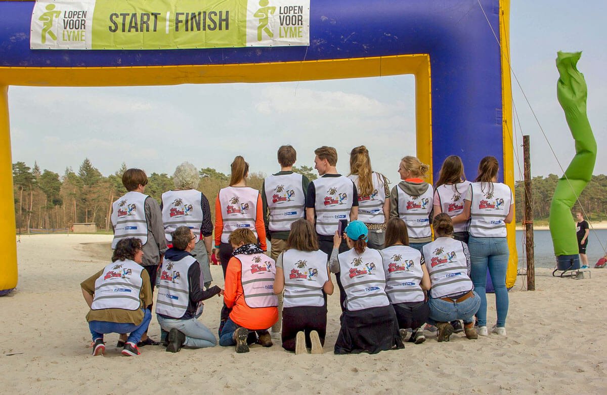 Groepsfoto loopteam Kick Mr. Tick bij de start/finish van Lopen voor Lyme Groepsfoto loopteam Kick Mr. Tick met hesjes bij de start/finish van Lopen voor Lyme